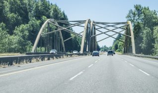 A driver's eye view traveling south on Interstate 5 in Washington state, part of the Pacific Northwest. It is a warm summer day. This part of the freeway is about half way between Seattle and Portland, Oregon. Brand names and logos have been removed from vehicles or are discernible. Blue sky and wispy clouds provide plenty of copy space.
